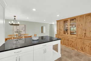 Kitchen with dark stone counters, glass insert cabinets, suspended lighting, and dual tone cabinetry