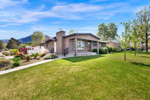 Rear view of house featuring a yard, stucco siding, and a chimney