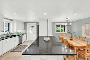 Kitchen featuring dark stone countertops, healthy amount of natural light, stainless steel dishwasher, and white cabinetry