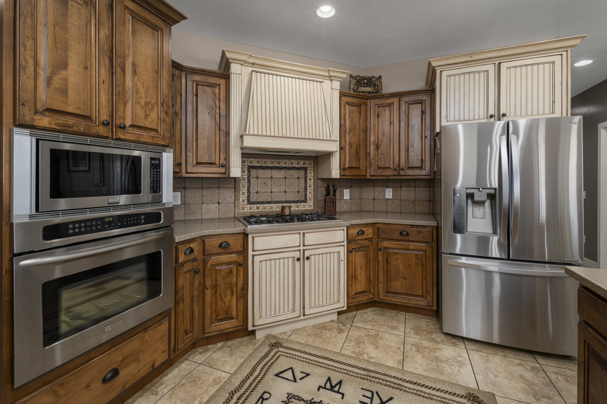 Kitchen featuring stainless steel appliances, tasteful backsplash, wood finish cabinets, light tile patterned flooring, and recessed lighting