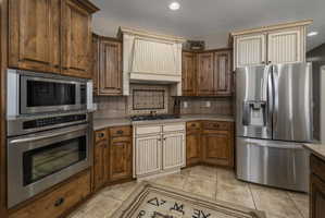 Kitchen featuring stainless steel appliances, tasteful backsplash, wood finish cabinets, light tile patterned flooring, and recessed lighting