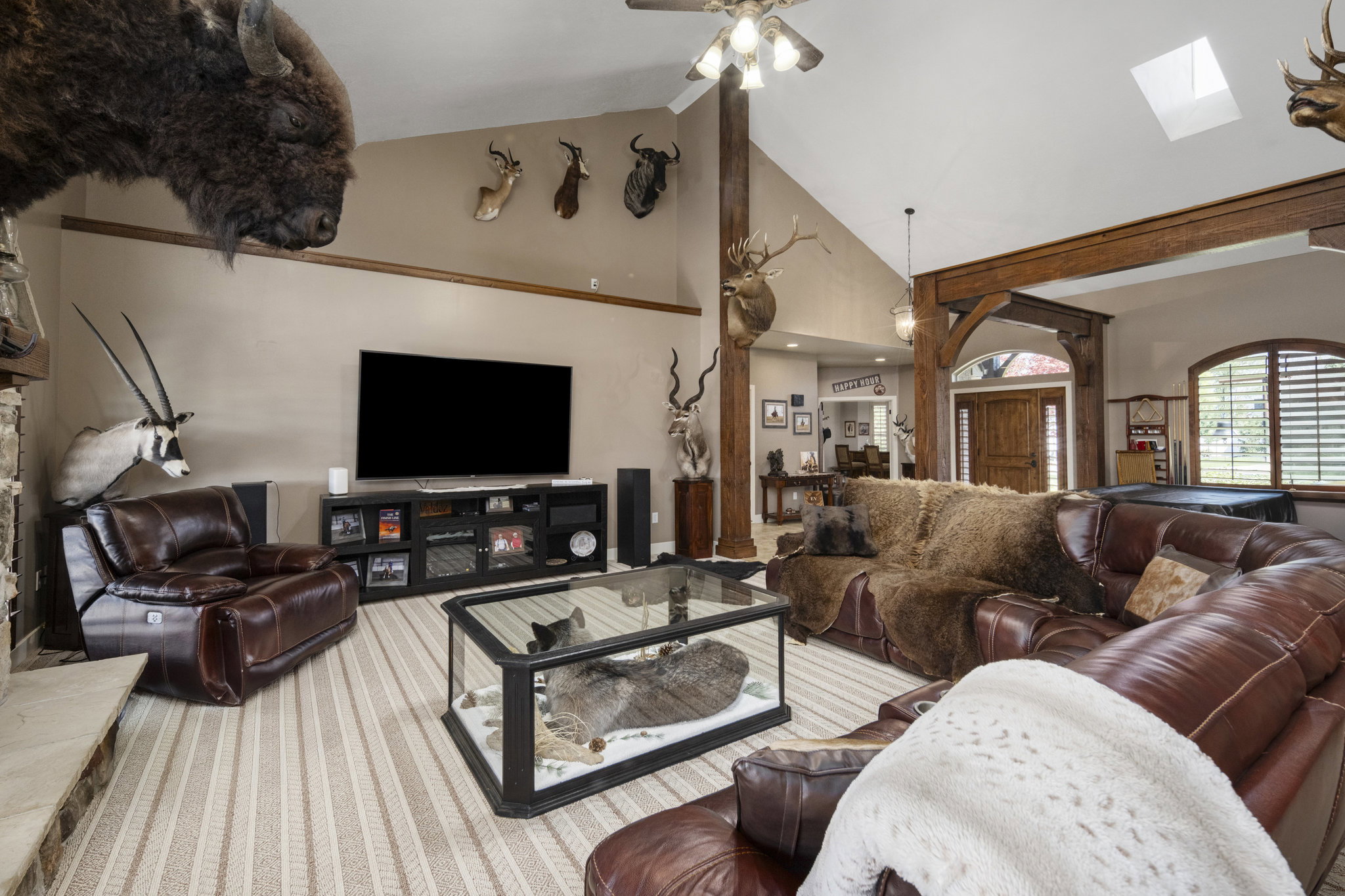 Living room featuring vaulted ceiling, ceiling fan, a fireplace with raised hearth, and a skylight