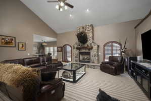 Carpeted living area featuring a ceiling fan, lofted ceiling, and a stone fireplace