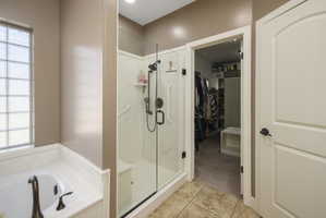 Full bath featuring a walk in closet, a bath, a shower stall, light colored carpet, and light tile patterned floors