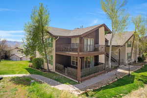 Rear view of property featuring a lawn, stucco siding, a deck, and roof with shingles