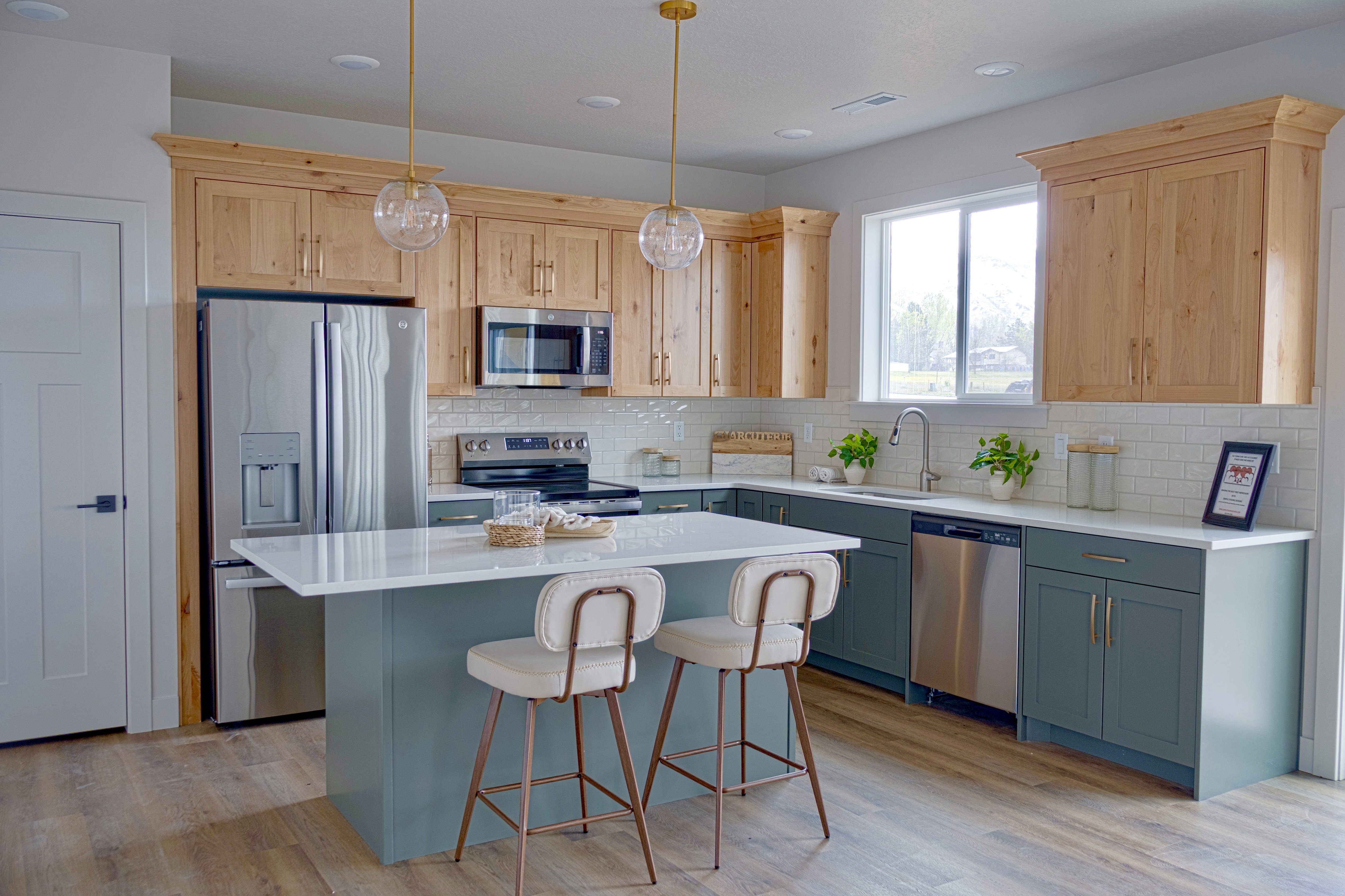 Contemporary kitchen featuring wood-finish flooring, two-tone cabinetry, stainless steel appliances, a white subway tile backsplash, and a central island with a solid surface countertop