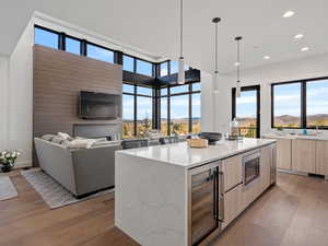 Kitchen featuring modern cabinets, light stone counters, beverage cooler, light wood finish cabinetry, and light wood-style flooring