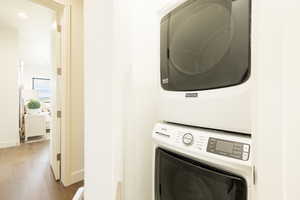 Laundry area featuring wood finished floors, stacked washer / dryer, and recessed lighting