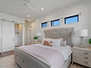 Bedroom with a barn door, a spacious closet, ceiling fan, recessed lighting, and wood finished floors