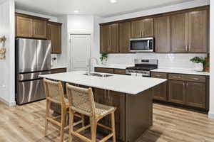 Kitchen featuring stainless steel appliances, a kitchen bar, an island with sink, dark wood finish cabinetry, and recessed lighting