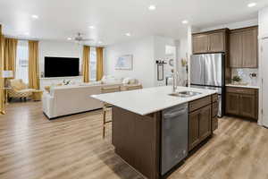 Kitchen with stainless steel appliances, ceiling fan, open floor plan, a kitchen island with sink, and light wood-style floors