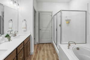 Full bath with double vanity, a stall shower, light wood-type flooring, and a bath