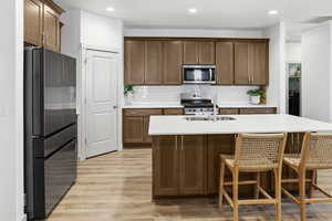 Kitchen with stainless steel appliances, a breakfast bar area, light wood finished floors, an island with sink, and recessed lighting