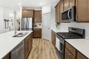 Kitchen featuring stainless steel appliances, light wood-type flooring, light stone counters, tasteful backsplash, and wood finish cabinets