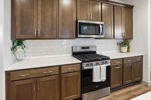 Kitchen with stainless steel appliances, light wood finished floors, decorative backsplash, and dark wood finish cabinetry
