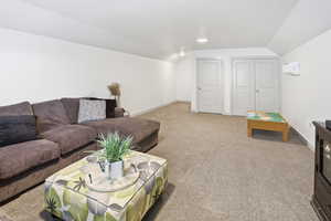 Carpeted living area featuring vaulted ceiling and baseboards