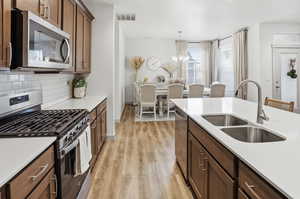 Kitchen featuring stainless steel appliances, light wood-type flooring, tasteful backsplash, light stone countertops, and suspended lighting