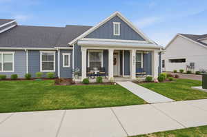 Modern farmhouse style home with covered porch, board and batten siding, a front yard, a shingled roof, and a metal roof