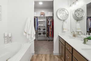 Full bath featuring a spacious closet, double vanity, a bath, and light wood-style floors