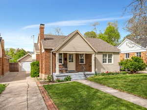 Bungalow with covered porch, an outbuilding, brick siding, a garage, and a front lawn