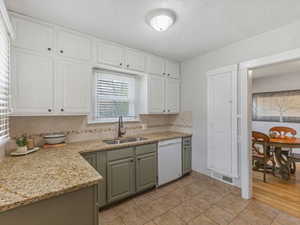 Kitchen featuring white dishwasher, light stone counters, backsplash, dual tone cabinets, and light tile patterned flooring