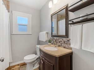 Bathroom featuring vanity, decorative backsplash, a shower with shower curtain, and light stone finish flooring