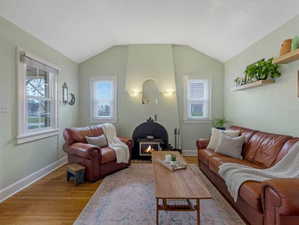 Living room with wood finished floors, lofted ceiling, and a lit fireplace