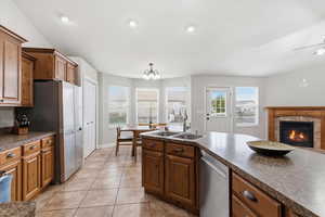 Kitchen featuring a fireplace, dark countertops, stainless steel appliances, light tile patterned floors, and hanging lights
