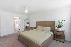 Carpeted bedroom featuring a ceiling fan, wood walls, and ensuite bath
