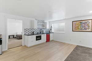 Kitchen with white cabinetry, light wood-style flooring, tasteful backsplash, and dark countertops