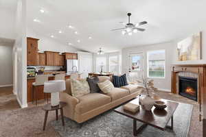 Living room featuring light carpet, a tiled fireplace, a chandelier, a ceiling fan, and vaulted ceiling