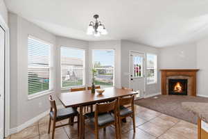 Dining space with a tiled fireplace, hanging lights, light tile patterned flooring, and light carpet