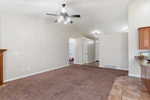 Unfurnished living room featuring light colored carpet, lofted ceiling, ceiling fan, and light tile patterned floors