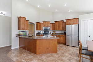 Kitchen featuring stainless steel appliances, wood finish cabinets, a peninsula, light tile patterned floors, and vaulted ceiling