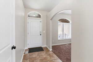Entrance foyer with light tile patterned floors, light colored carpet, and arched walkways