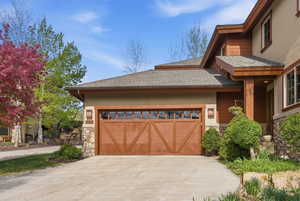 View of property exterior with stone siding, roof with shingles, driveway, a garage, and stucco siding
