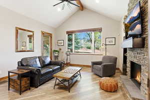 Living area with ceiling fan, a stone fireplace, and wood finished floors