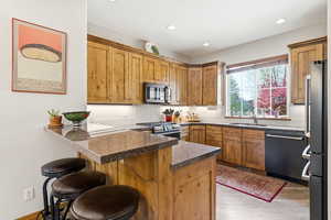Kitchen with wood finish cabinets, a peninsula, stainless steel appliances, a breakfast bar, and light wood-type flooring