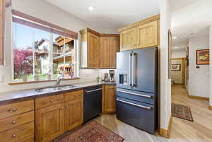 Kitchen with high quality fridge, dishwasher, dark stone counters, light wood-style flooring, and wood finish cabinets