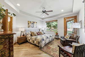 Bedroom with light wood finished floors, a raised ceiling, ceiling fan, recessed lighting, and access to outside