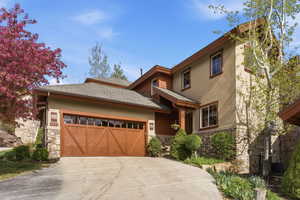 View of front of home with stone siding, a shingled roof, a garage, concrete driveway, and stucco siding