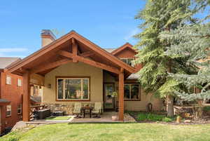 Rear view of property with a chimney, a lawn, a patio, and stucco siding