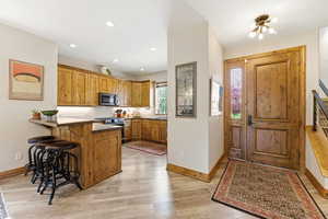 Kitchen with a kitchen bar, light wood-style flooring, a peninsula, stainless steel appliances, and wood finish cabinetry