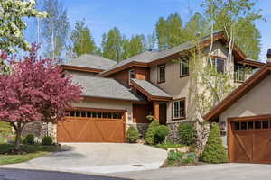 View of front of house featuring stone siding, a shingled roof, an attached garage, concrete driveway, and stucco siding