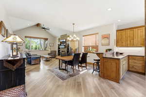 Dining area featuring ceiling fan, light wood finished floors, hanging lights, and vaulted ceiling