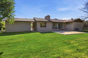 Back of property featuring brick siding, a lawn, a chimney, and roof with shingles