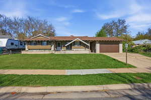 Ranch-style house with a garage, concrete driveway, brick siding, board and batten siding, and a front yard