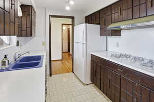 Kitchen featuring dark wood finish cabinets, light countertops, white appliances