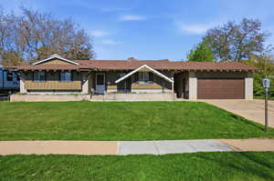 View of front of home featuring board and batten siding, brick siding, a garage, a front yard, and driveway