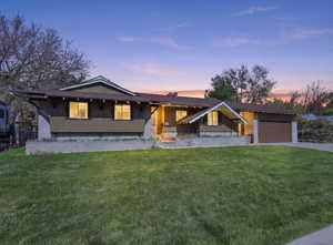 View of front of house with board and batten siding, a yard, driveway, and brick siding